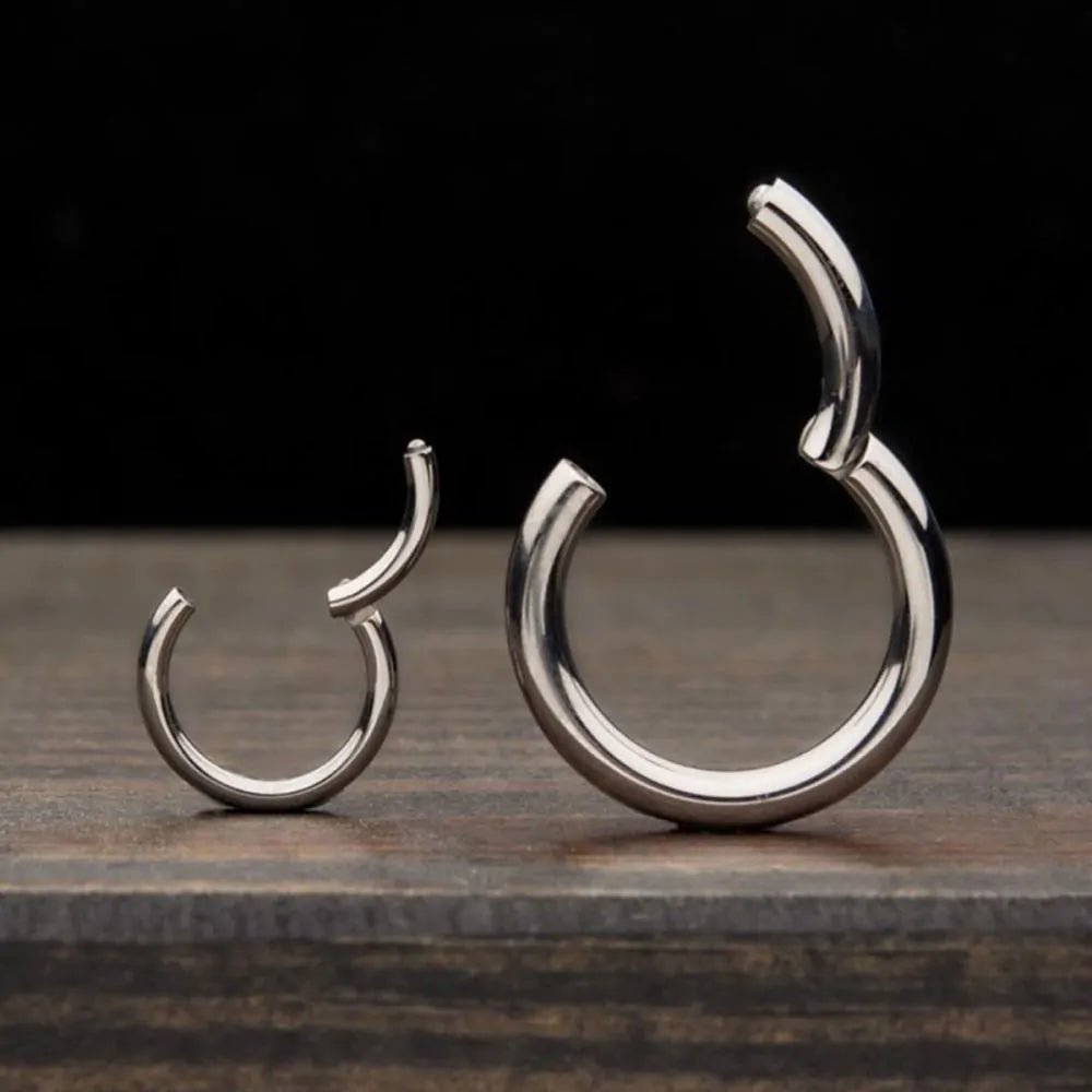Pair of titanium clicker hinge hoop earrings on a wooden surface with a dark background